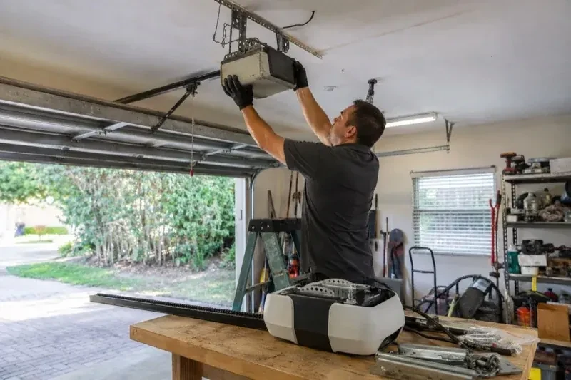 Person holding an overhead garage-door opener beside another opener and hardware on a workbench — Garage Door Opener Replacement, Georgina