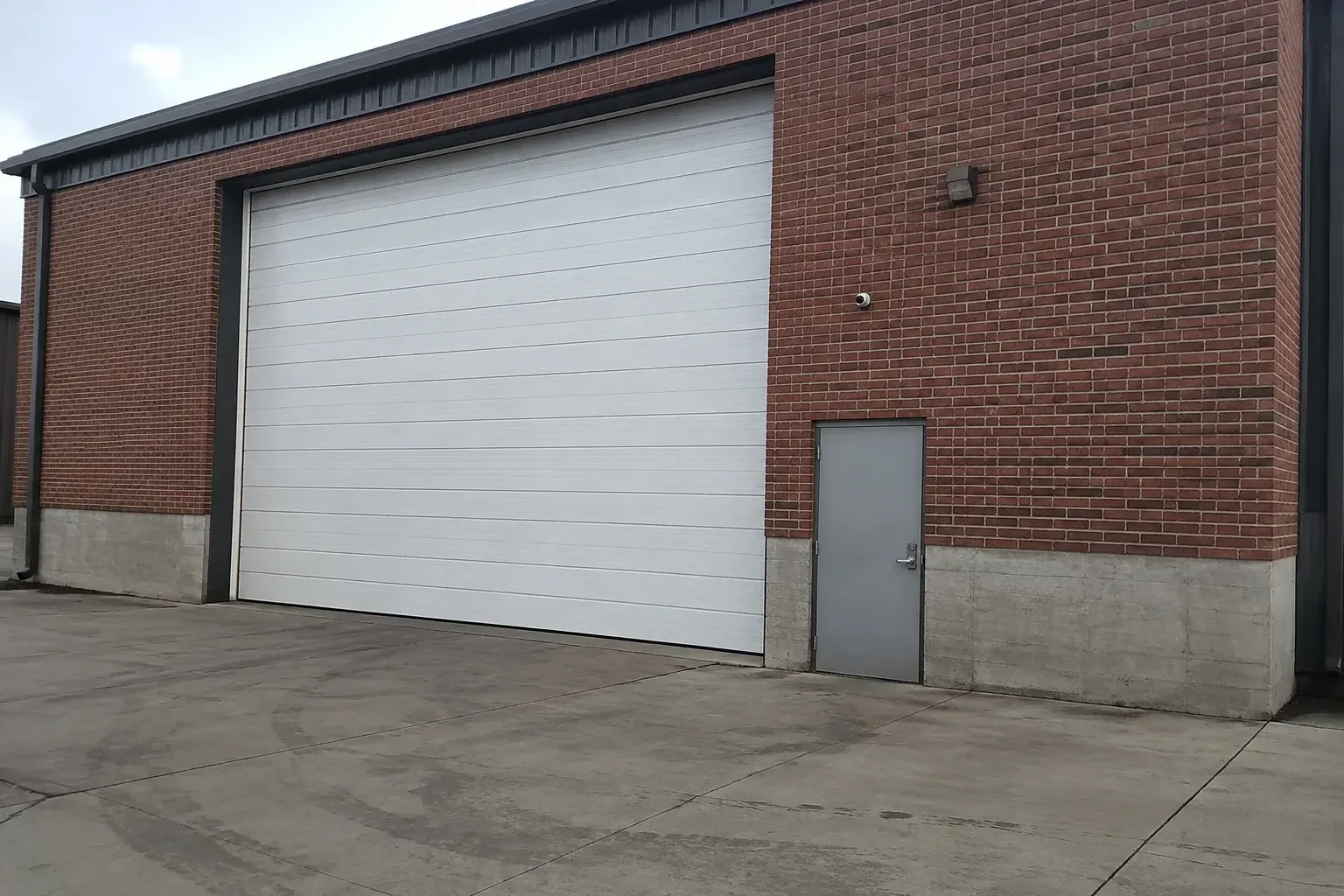 Tall closed sectional loading door beside a personnel door at a brick unit. — Commercial Sectional Door Repair, Cannington
